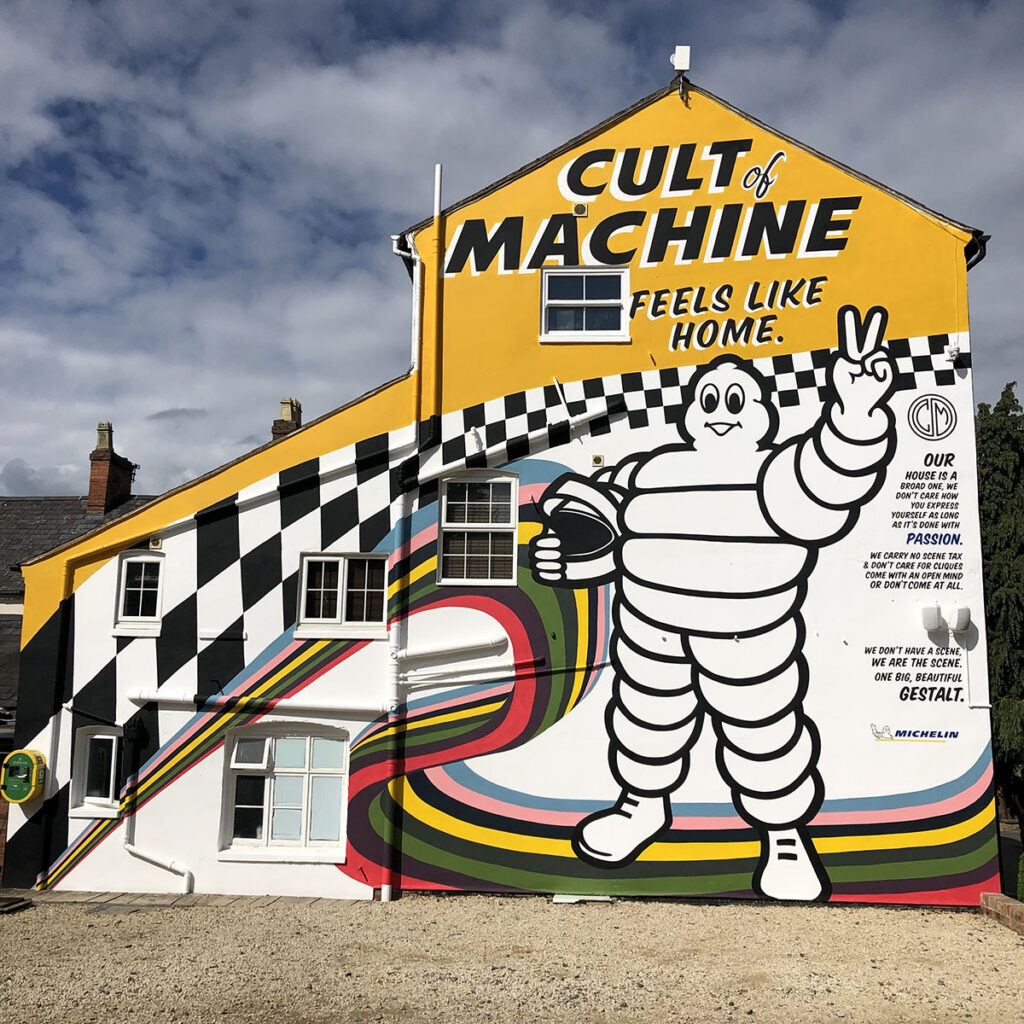 Large hand-painted mural for Caffeine & Machine featuring the Michelin Man, bold racing colours and checkerboard graphics across the full side of the building.
