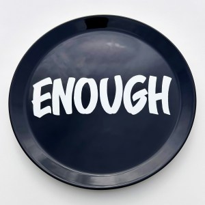 Hand painted black ceramic plate with the word ENOUGH hand lettered in white on wall as a black and white interior decor statement piece