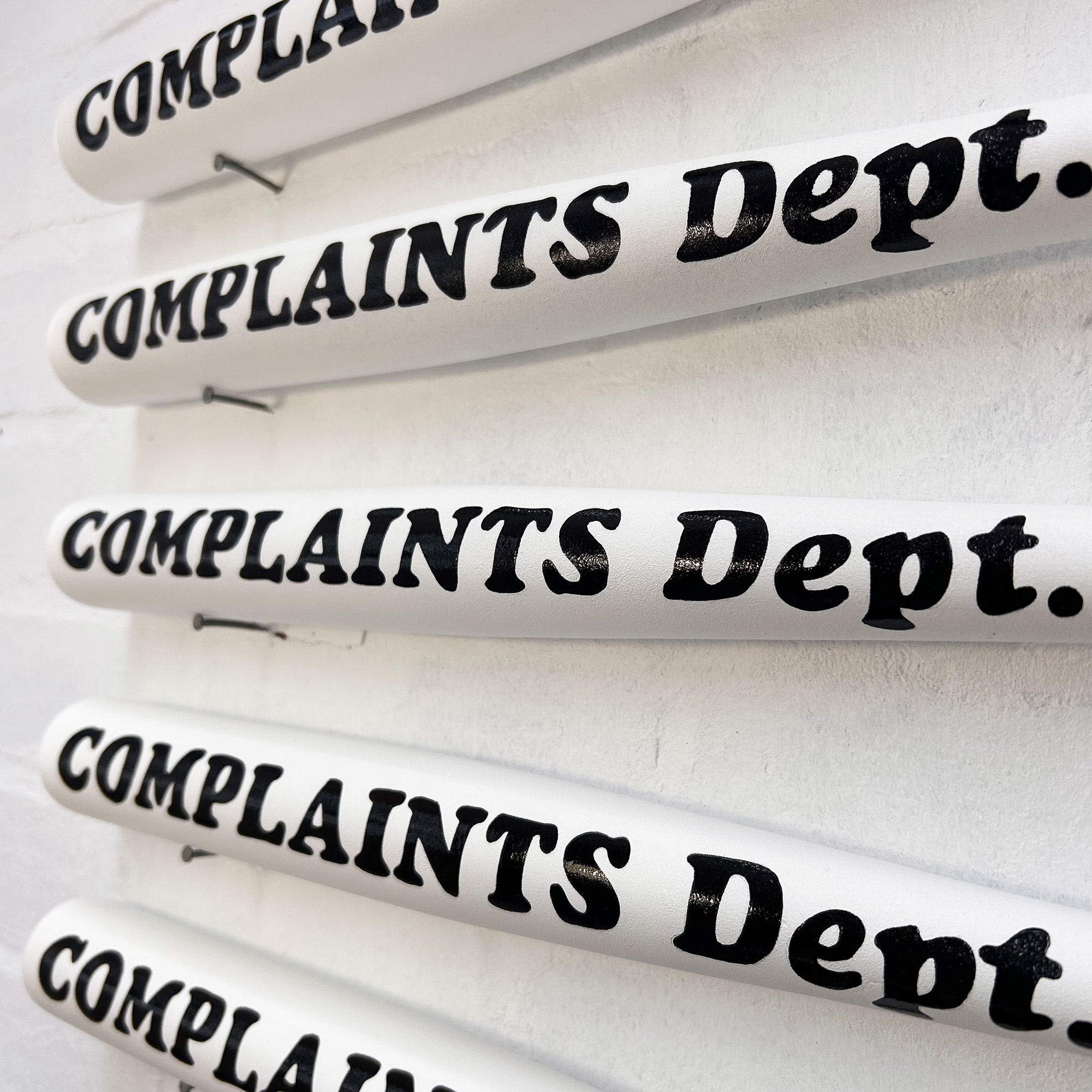 Close up of black hand painted Complaints Dept lettering on white bat