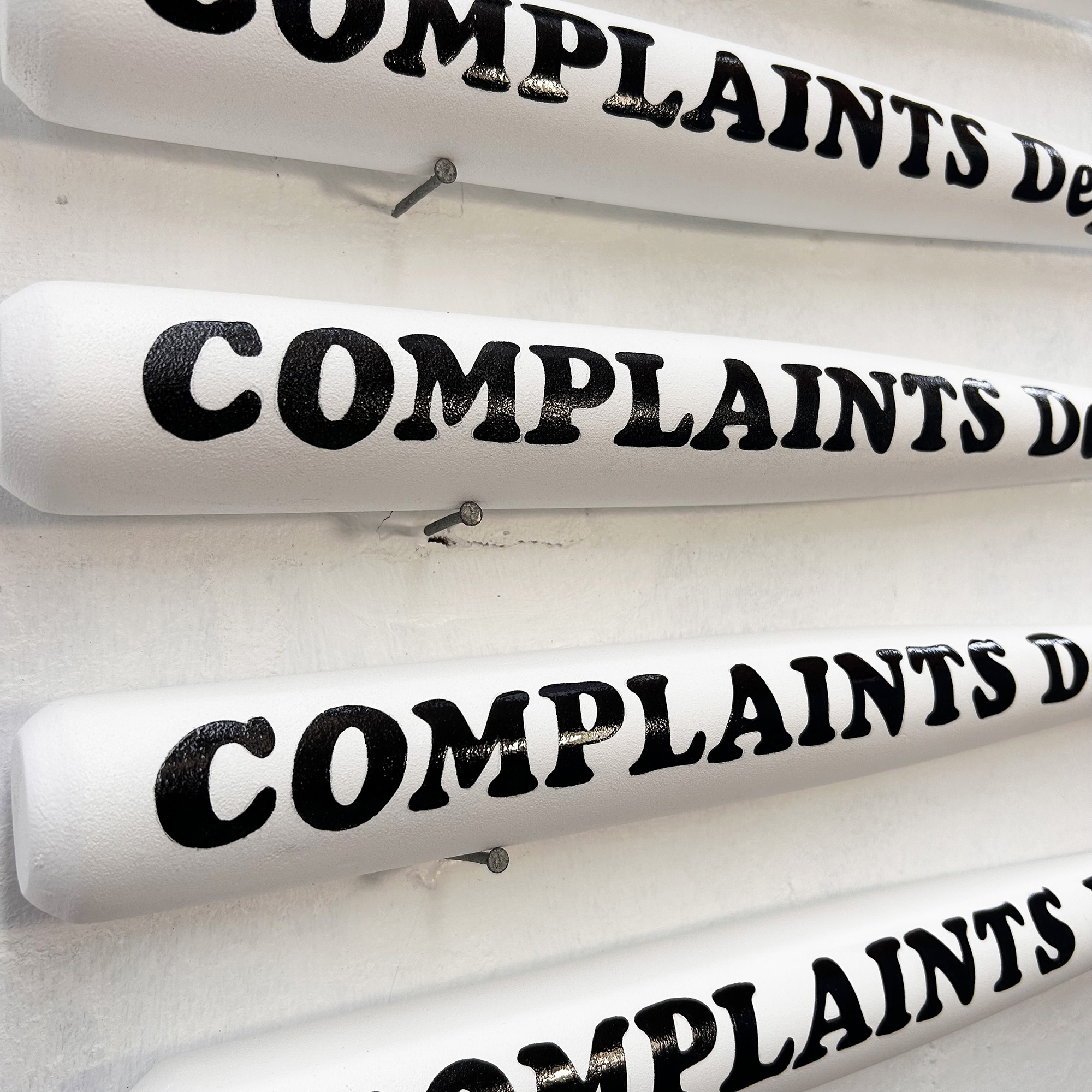 Detailed photo of black sign written Complaints Dept lettering on white bat.